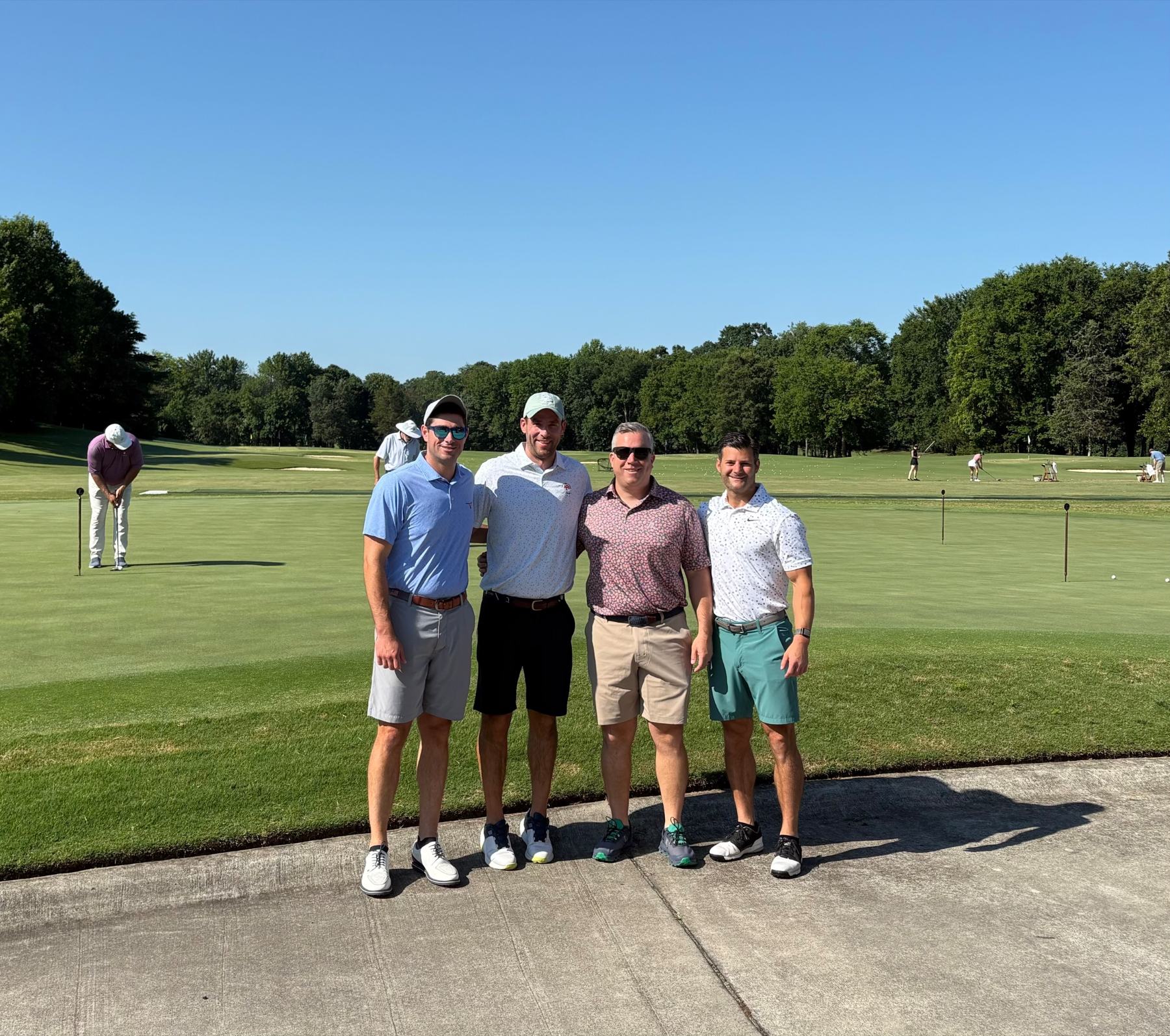 A foursome in golf polos posing beside the practice green on a sunny morning