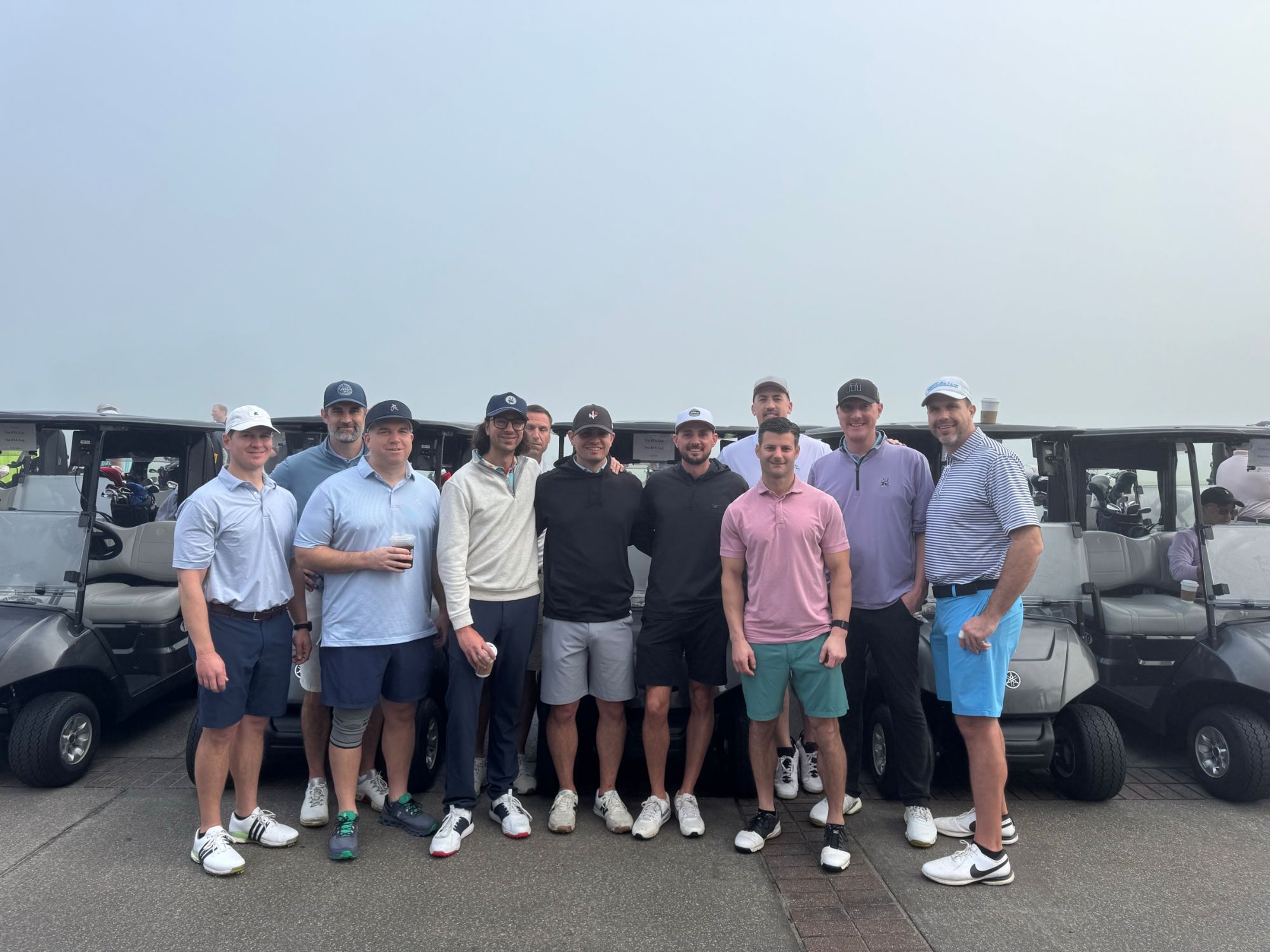 Golfers gathered in front of a row of carts on a foggy morning before a shotgun start